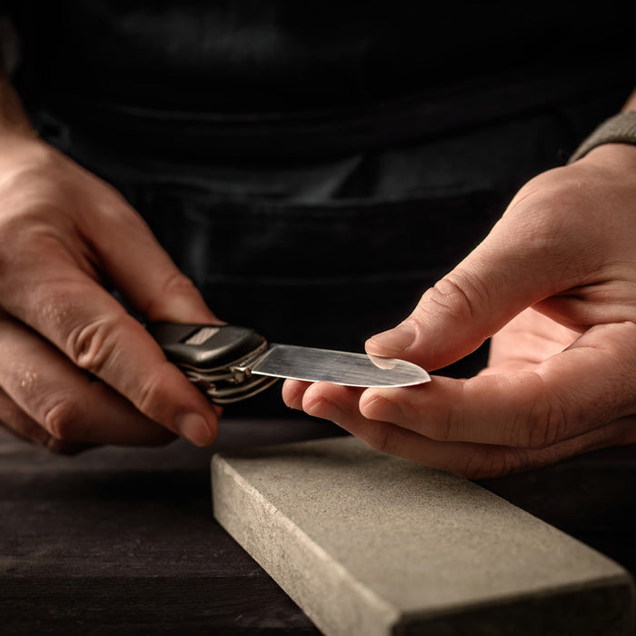Close shot of a man holding a pocket knife above a tan whetstone for sharpening.