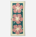 A rectangular woven textile with a cream border and three large pink hibiscus flowers on a dark teal background, shown flat against a light gray studio backdrop.