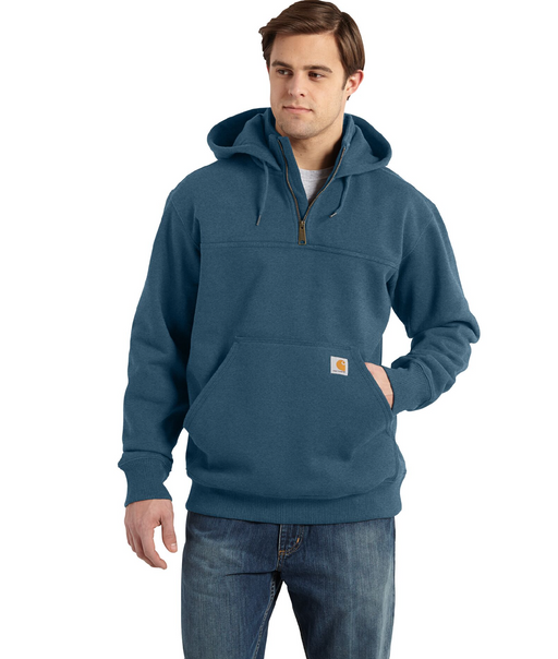 A man wearing a blue quarter-zip pullover hoodie with a kangaroo pocket and a small Carhartt logo patch, paired with blue jeans, against a plain white background.