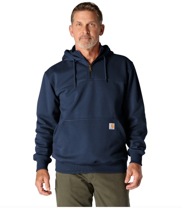 A man wearing a navy blue Carhartt quarter-zip pullover hoodie with a drawstring hood and a front kangaroo pocket, paired with olive green pants, against a plain white background.