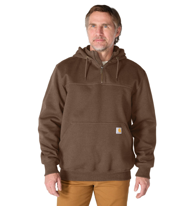 A man wearing a brown pullover hoodie with a half-zip neckline, drawstrings, and a small Carhartt logo patch on the pocket, paired with tan pants against a white background.