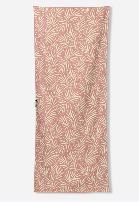 A rectangular beach towel with a repeating palm leaf pattern in cream on a dusty rose background, shown flat against a light gray studio background.