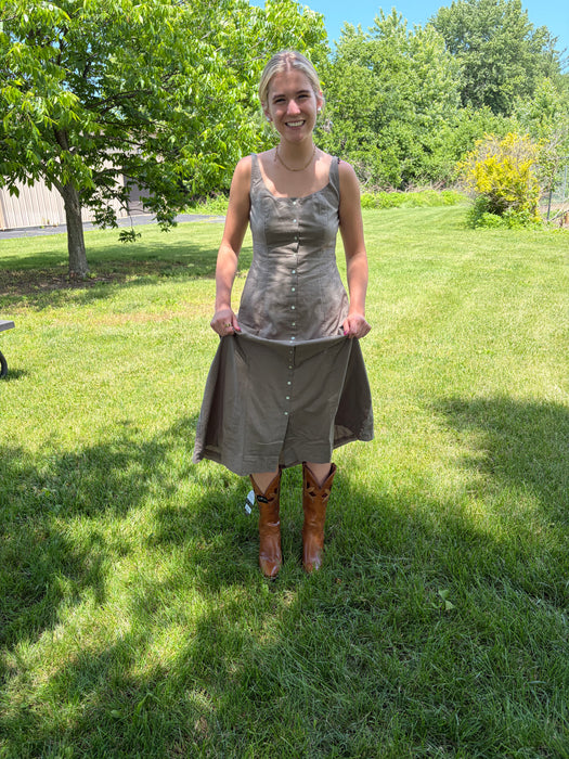 Woman standing in a grassy area wearing a dress and boots.
