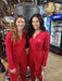 Two women smiling and wearing matching red Carhartt union suits, standing in a store with various items on the shelves in the background.