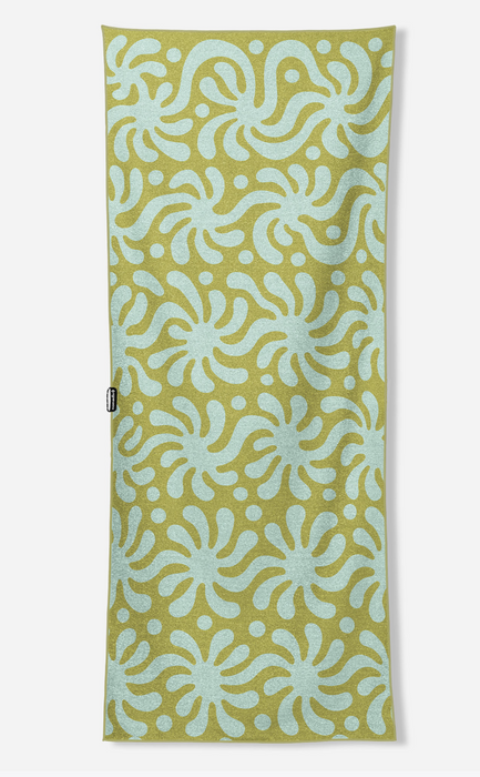 A long rectangular towel with a repeating abstract floral or starburst pattern in pale aqua on a muted yellow-green background, shown flat against a light gray studio background.