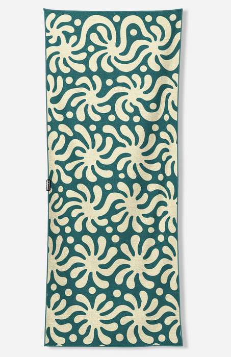 A rectangular fabric item, likely a towel or blanket, featuring a repeating cream-colored abstract floral or starburst pattern on a dark teal-green background.