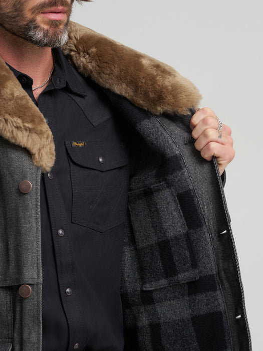 Man wearing a dark coat with a fur-lined hood against a light gray background